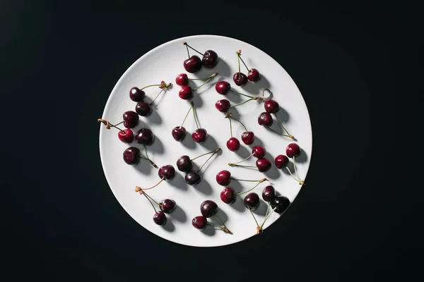 Top view of fresh ripe red cherries on round white plate isolated on black — Stock Photo