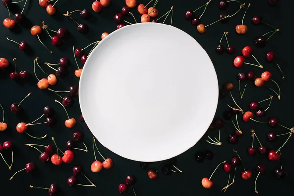 Top view of empty round white plate and sweet cherries on black — Stock Photo