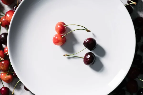 Vista superior de cerezas rojas y amarillas maduras sobre plato blanco - foto de stock