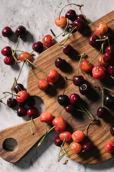 Vue de dessus des cerises douces mûres fraîches sur la planche à découper en bois sur la surface du marbre — Photo de stock