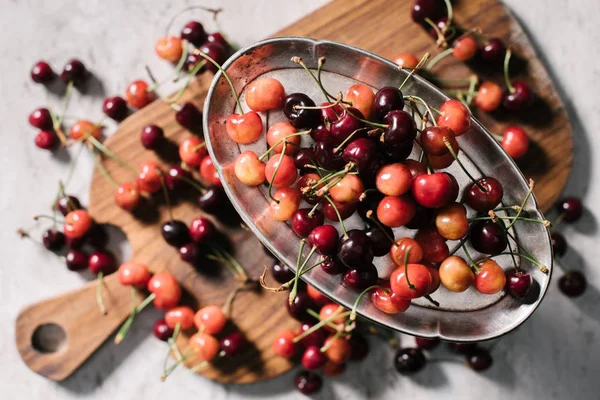 Vue du dessus des cerises mûres sucrées sur plaque vintage et planche à découper en bois sur foyer blanc et sélectif — Photo de stock