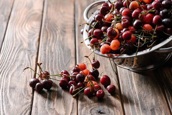 Colander with fresh ripe sweet cherries on wooden table — Stock Photo