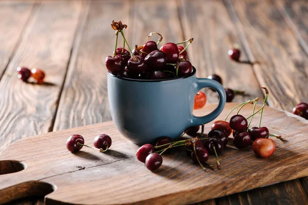 Close-up view of ripe fresh sweet cherries in blue cup on wooden cutting board on table — Stock Photo