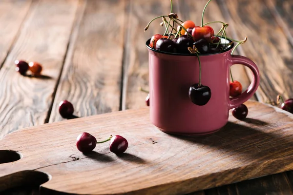 Close-up view of organic sweet cherries in pink cup on wooden cutting board on table — Stock Photo