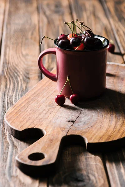 Healthy tasty cherries in pink cup on wooden cutting board on table — Stock Photo