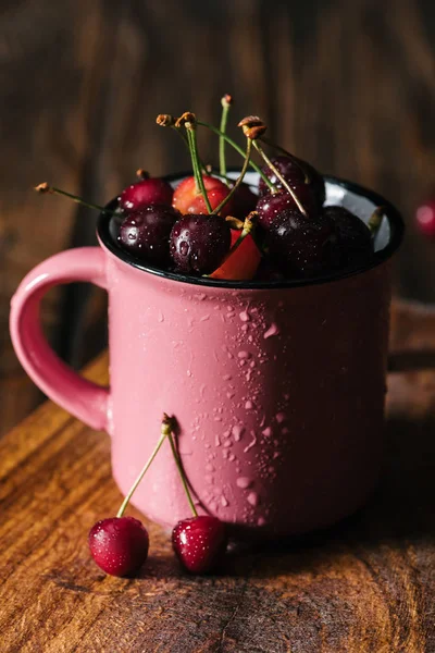 Крупним планом вид на свіжі стиглі вишні в мокрій рожевій чашці на дерев'яному столі — стокове фото
