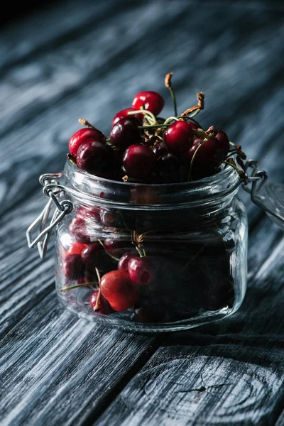 Close-up view of fresh ripe cherries in glass jar on rustic wooden table — Stock Photo