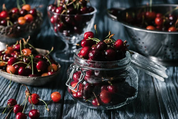 Vista de cerca de cerezas frescas maduras en frasco de vidrio, colador y utensilios en mesa de madera rústica - foto de stock