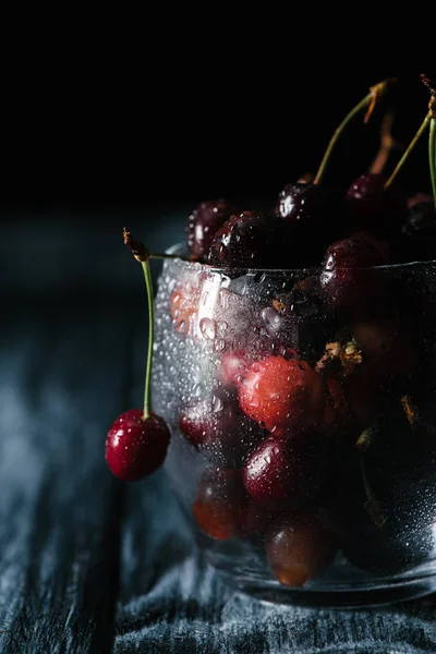 Nahaufnahme reifer Süßkirschen im nassen Glas auf Holztisch — Stockfoto