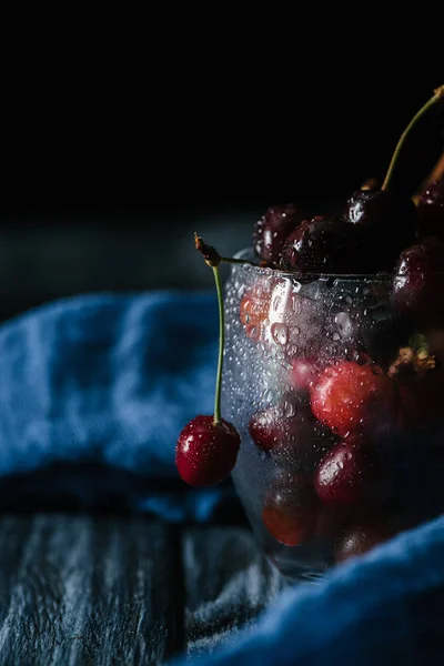 Ripe sweet organic cherries in wet glass on wooden table — Stock Photo