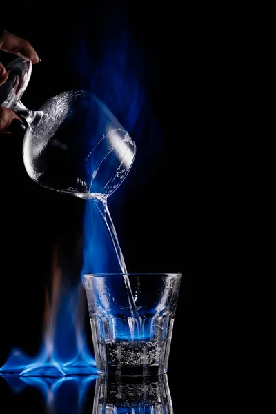 Vue partielle de la femme versant une boisson alcoolisée sambuca brûlante dans un verre sur fond noir — Photo de stock
