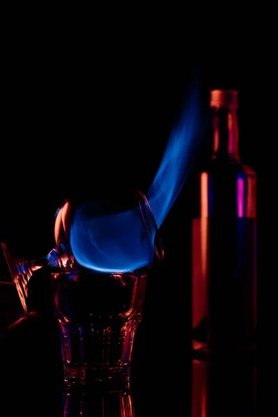 Primer plano vista de alcohol sambuca bebida quema en vidrio sobre fondo negro - foto de stock