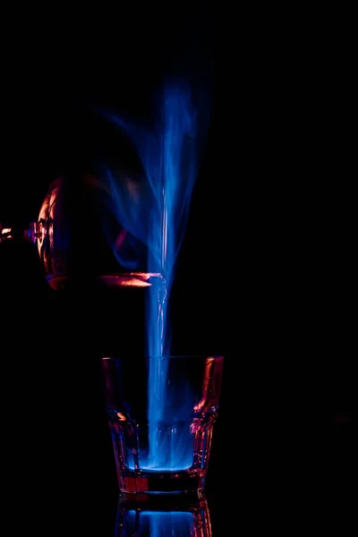 Close up view of pouring burning sambuca alcohol drink into glass process on black background — Stock Photo