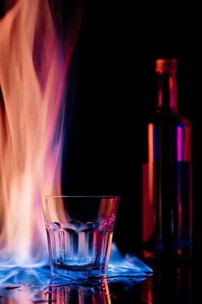 Vue rapprochée de la flamme, verre vide et bouteille de boisson alcoolisée sambuca sur fond noir — Photo de stock