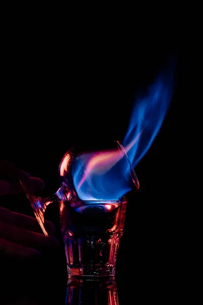 Vue partielle d'une femme tenant un verre avec une boisson alcoolisée sambuca brûlante sur fond noir — Photo de stock