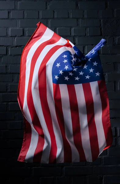 Vertikal schwenkt die Flagge der Vereinigten Staaten vor einer schwarzen Backsteinmauer, Konzept zum Unabhängigkeitstag — Stockfoto
