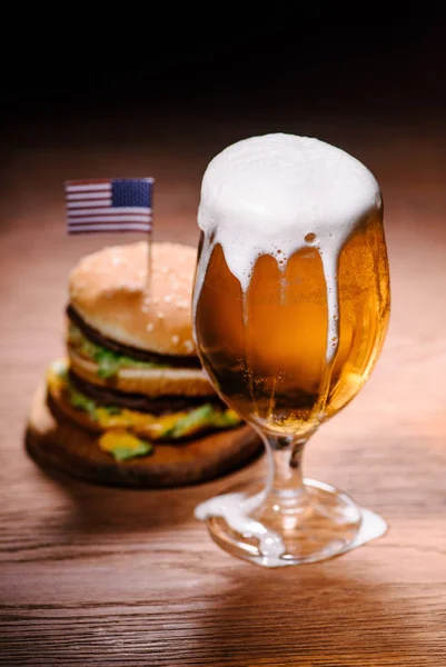 Tasty burger with glass of beer on wooden table — Stock Photo