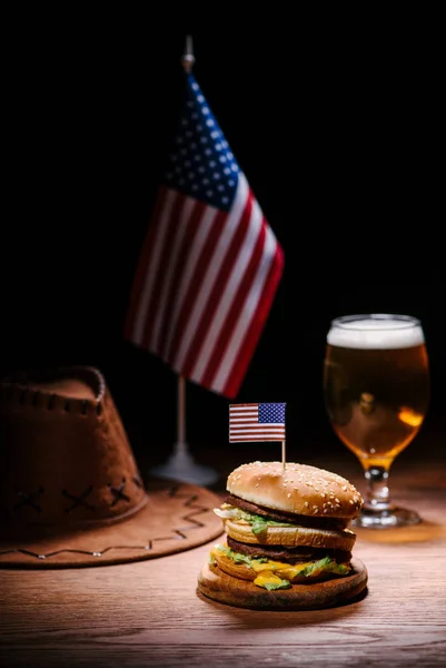 Вкусный бургер на деревянном столе в американской ковбойской шляпе, флаг США и бокал пива — стоковое фото