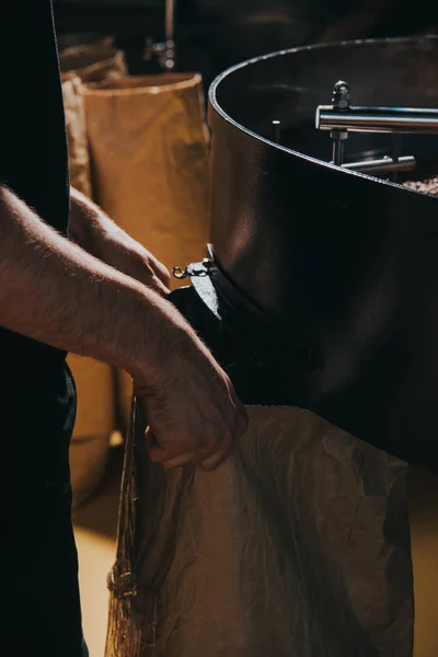 Mains masculines remplissant sac en papier avec des haricots fraîchement rôtis — Photo de stock