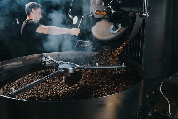 Professional male roaster loading container of steaming machine with coffee beans — Stock Photo