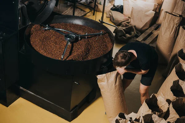 Homem saco de papel de enchimento com grãos de café recém-torrados — Fotografia de Stock