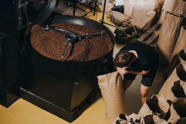 Man filling paper bag with freshly roasted coffee beans — Stock Photo