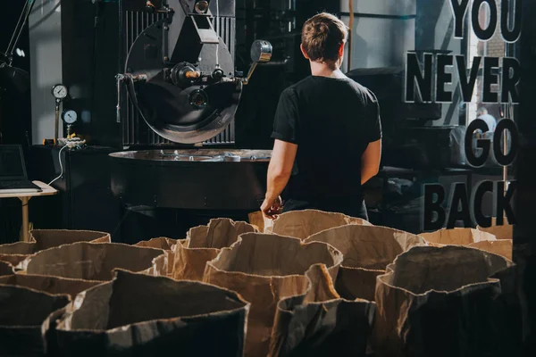 Homme debout par des sacs en papier avec des grains de café dans un café industriel — Photo de stock