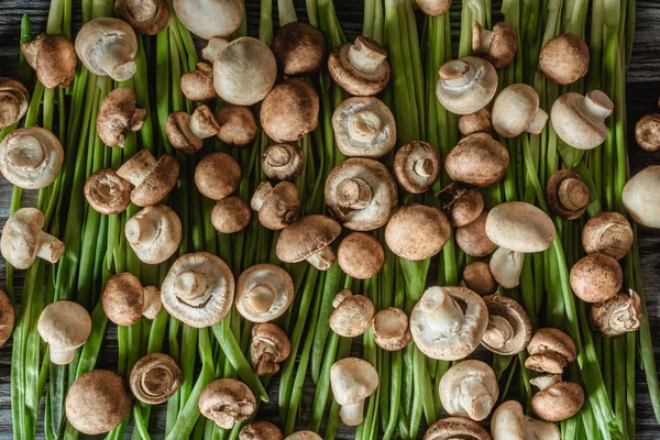 Top view of champignon mushrooms on green leeks on wooden tabletop — Stock Photo