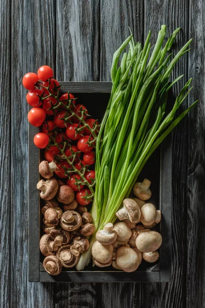 Top view of champignon mushrooms with leeks and cherry tomatoes in box on wooden tabletop — Stock Photo