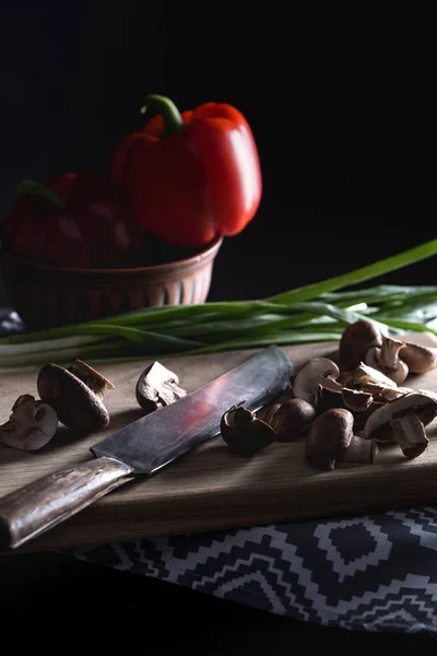 Close-up shot of raw sliced champignon mushrooms with knife on wooden cutting board on black — Stock Photo