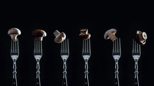 Row of champignon mushrooms on forks isolated on black — Stock Photo