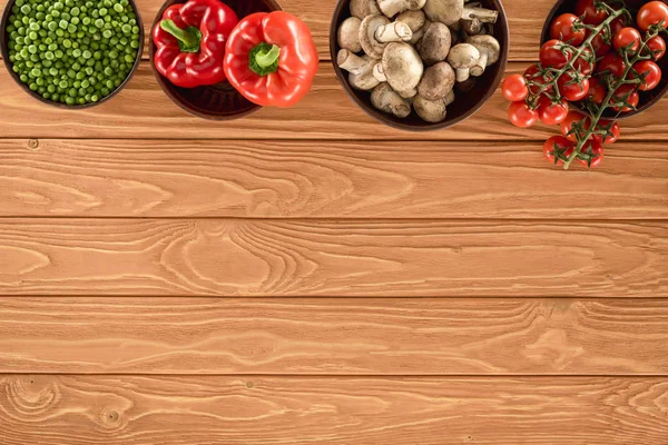Vista superior de cogumelos de champignon e vários vegetais em tigelas em mesa de madeira — Fotografia de Stock