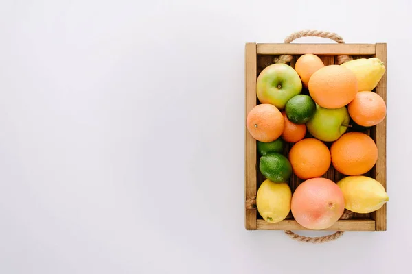 Вид зверху на різні стиглі фрукти в дерев'яній коробці на білій поверхні — стокове фото