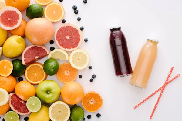 Top view of various citrus fruits and blueberries with bottles of juice on white tabletop — Stock Photo