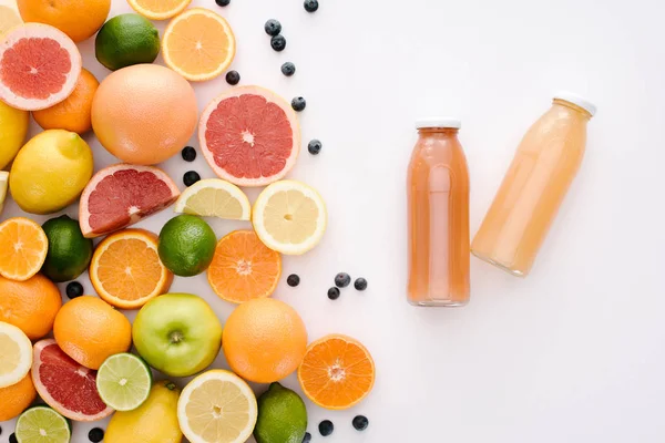 Top view of various citrus fruits with bottles of juice on white surface — Stock Photo