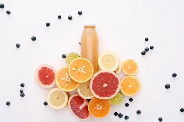 Vista superior de garrafa de suco com fatias de frutas cítricas e mirtilos na superfície branca — Fotografia de Stock
