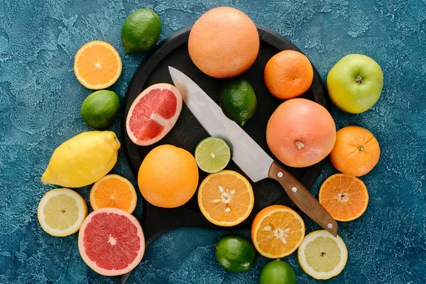 Top view of plate in shape of skillet and knife with citrus fruits slices on blue concrete surface — Stock Photo