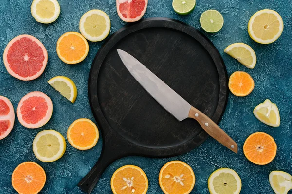 Top view of plate in shape of skillet and knife surrounded with citrus fruits slices on blue concrete surface — Stock Photo