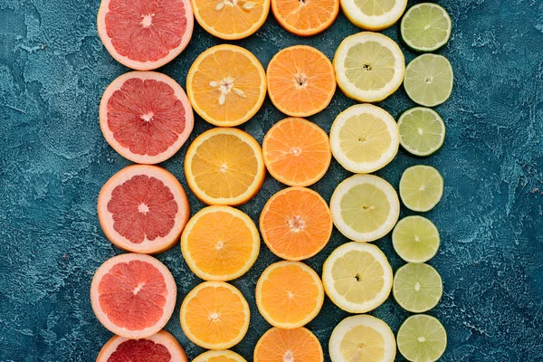 Vista superior de várias fatias de frutas cítricas em linhas na superfície de concreto azul — Fotografia de Stock