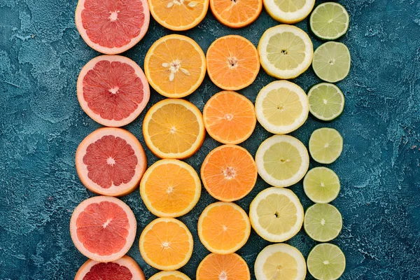 Top view of various citrus fruits slices in rows on blue concrete surface — Stock Photo