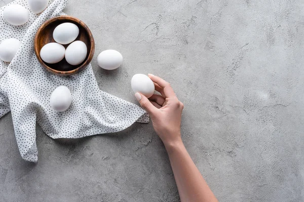 Vista parcial de la mano de la hembra y huevos crudos de pollo sobre la mesa gris - foto de stock