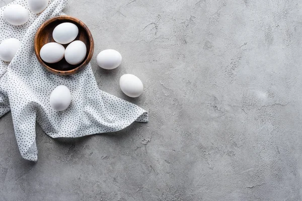 Flat lay with raw chicken eggs in bowl and linen on grey tabletop — Stock Photo