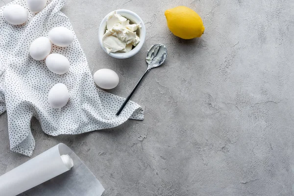La puesta plana con limón, crema agria en tazón y huevos crudos de pollo para pastel en la superficie gris - foto de stock