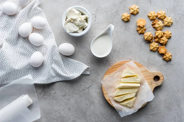 Flat lay with cut butter, sour cream, cookies and raw chicken eggs ingredients for making pie on grey surface — Stock Photo