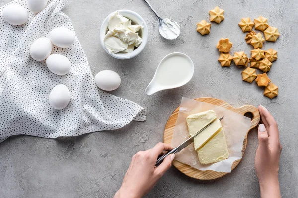 Colpo ritagliato di donna che taglia burro sul tagliere per torta fatta in casa sul tavolo grigio — Foto stock