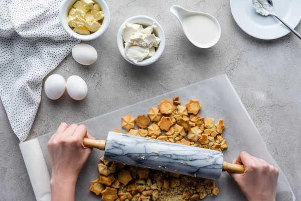 Vista parcial de la mujer aplastando galletas con rodillo para pastel en la mesa gris - foto de stock