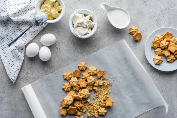 La puesta plana con galletas, huevos de pollo crudos, mantequilla y crema agria para hacer pastel arreglado en la mesa gris - foto de stock