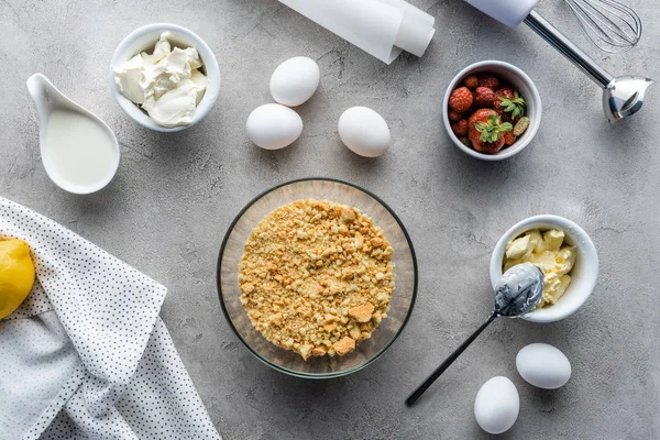 Vista dall'alto della pasta preparata per torta, fragole, uova di pollo crude e carta da forno su tavolo grigio — Foto stock