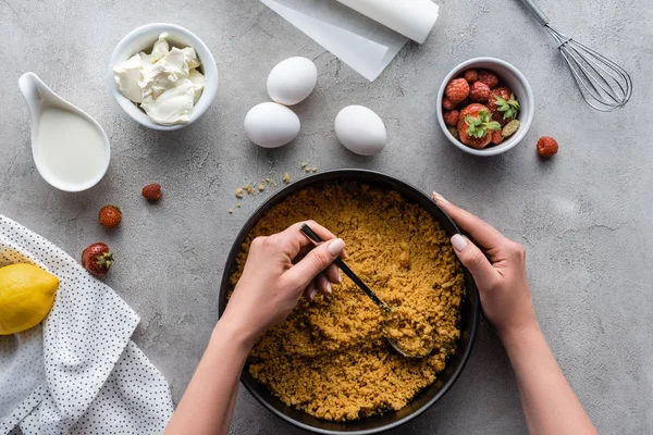 Visão parcial da mulher colocando massa de torta em forma de cozimento com ingredientes ao redor na superfície cinza — Fotografia de Stock