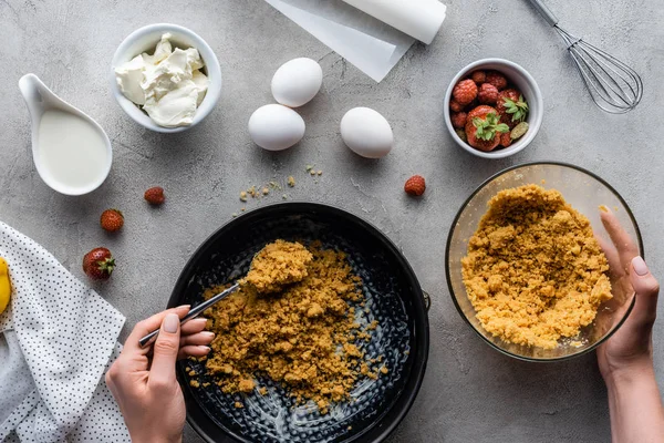 Visão parcial da mulher colocando massa de torta em forma de cozimento com ingredientes ao redor na superfície cinza — Fotografia de Stock